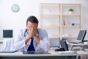 Doctor sitting at his desk with head in hands. 